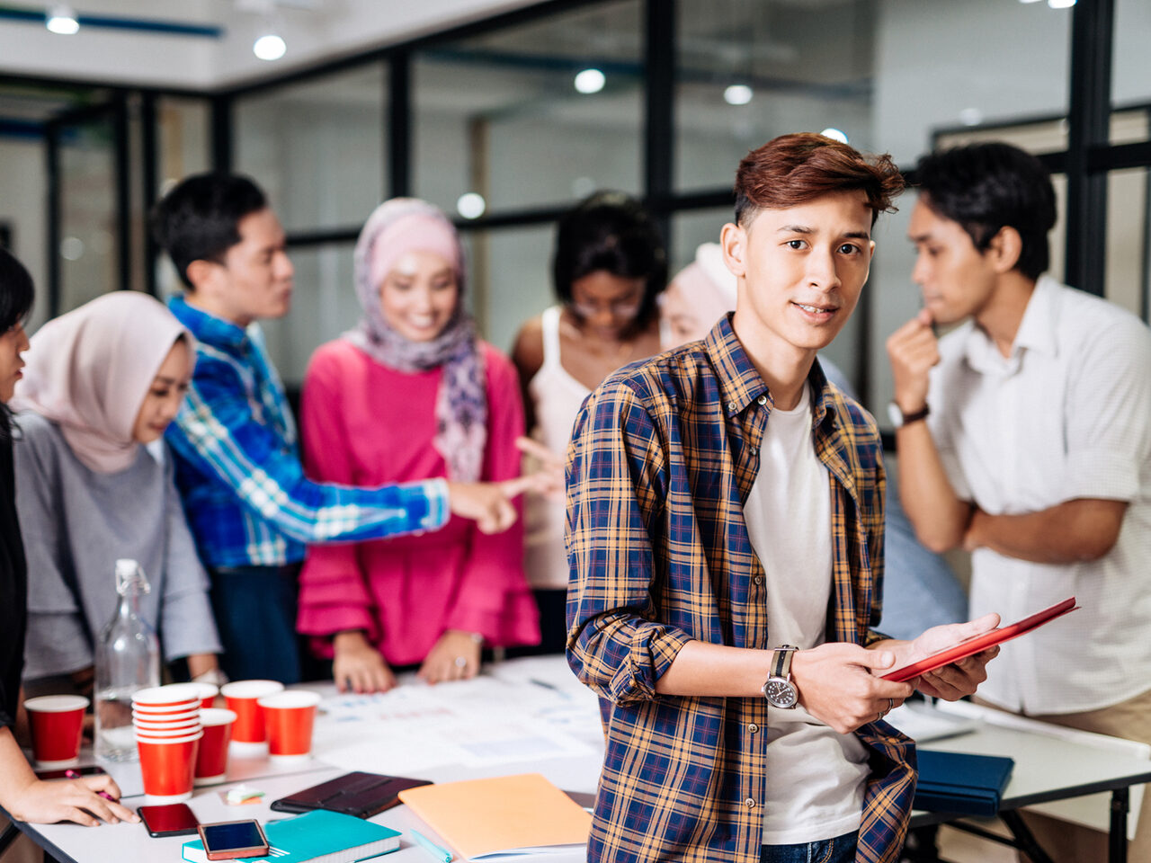 Junge Menschen unterschiedlichen Geschlechts und Hautfarbe stehen um einen Tisch herum und diskutieren Arbeitsergebnisse miteinander