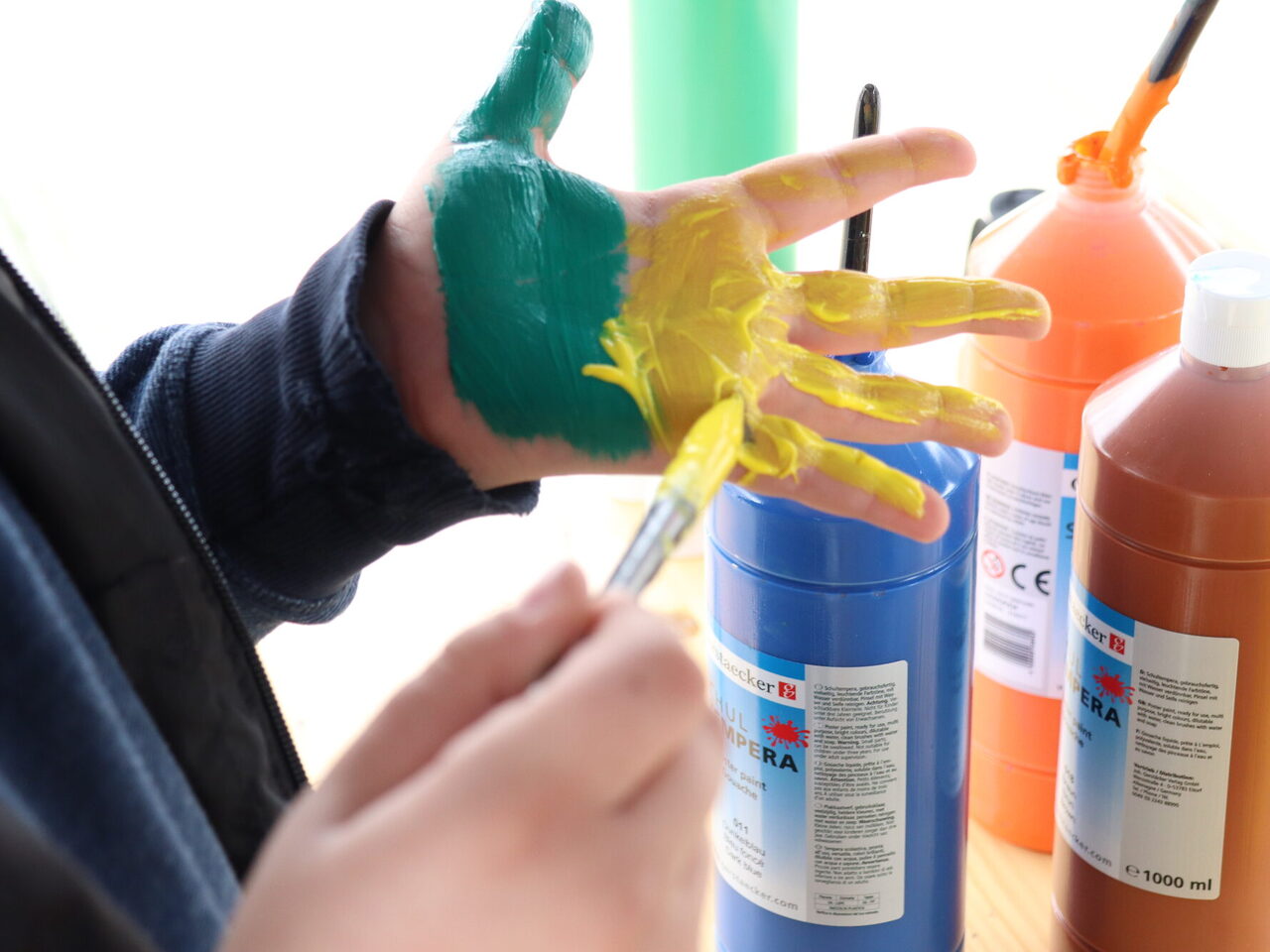 Ein Junge bemalt seine Hand mit gelber und grüner Farbe um einen Abdruck zu machen.