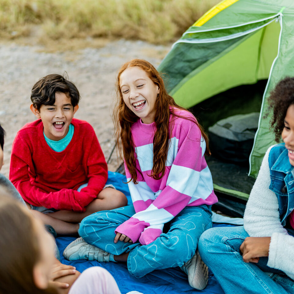 Kinder sitzen vor einem Zelt und lachen