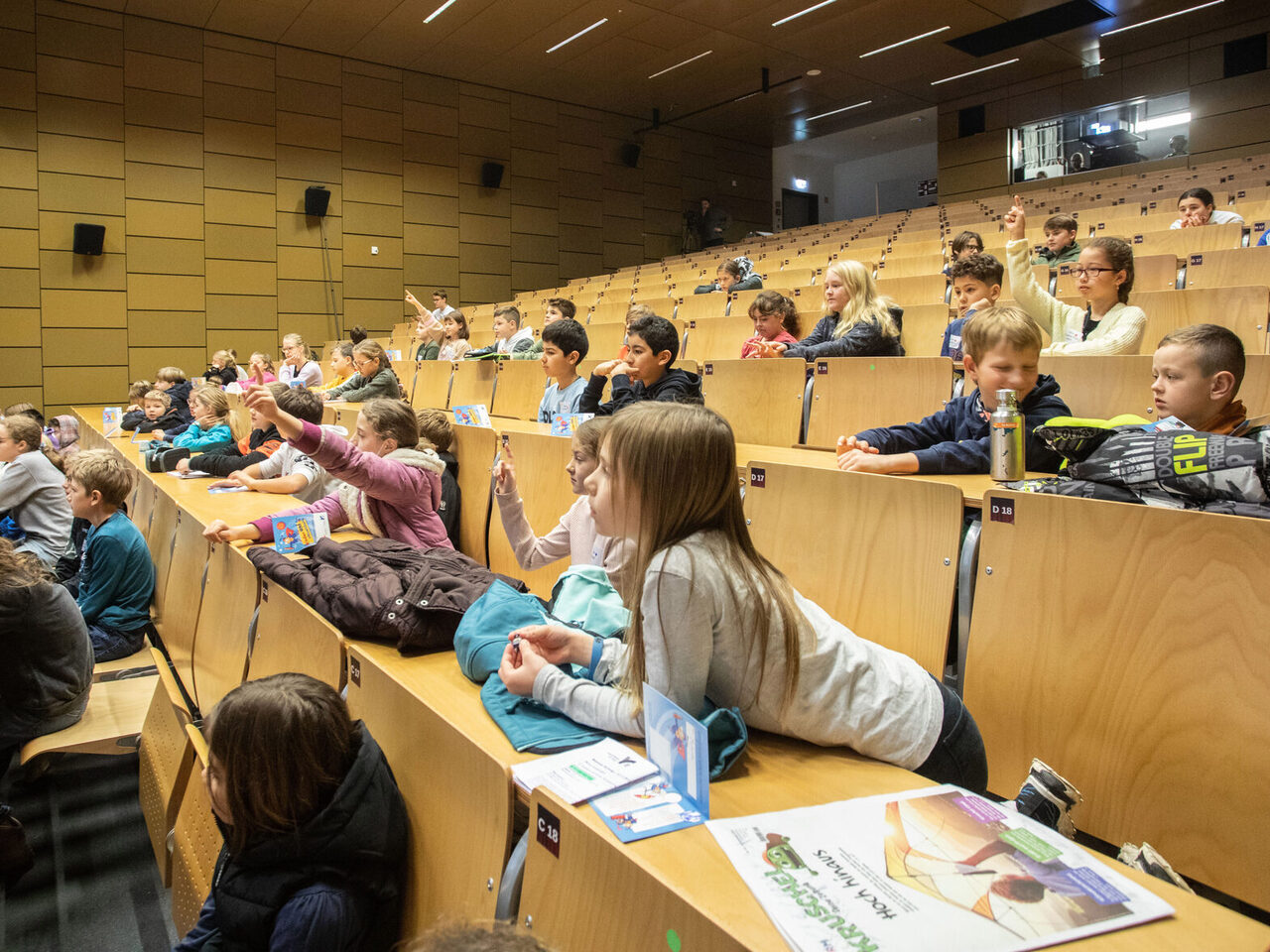 Zahlreiche Kinder hören in einem Stufenhörsaal interessiert einer Vorlesung zu